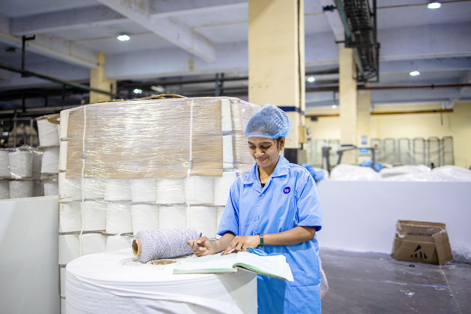 Factory worker recording production details in an Indian manufacturing plant, illustrating batch traceability required for food-grade paper packaging.