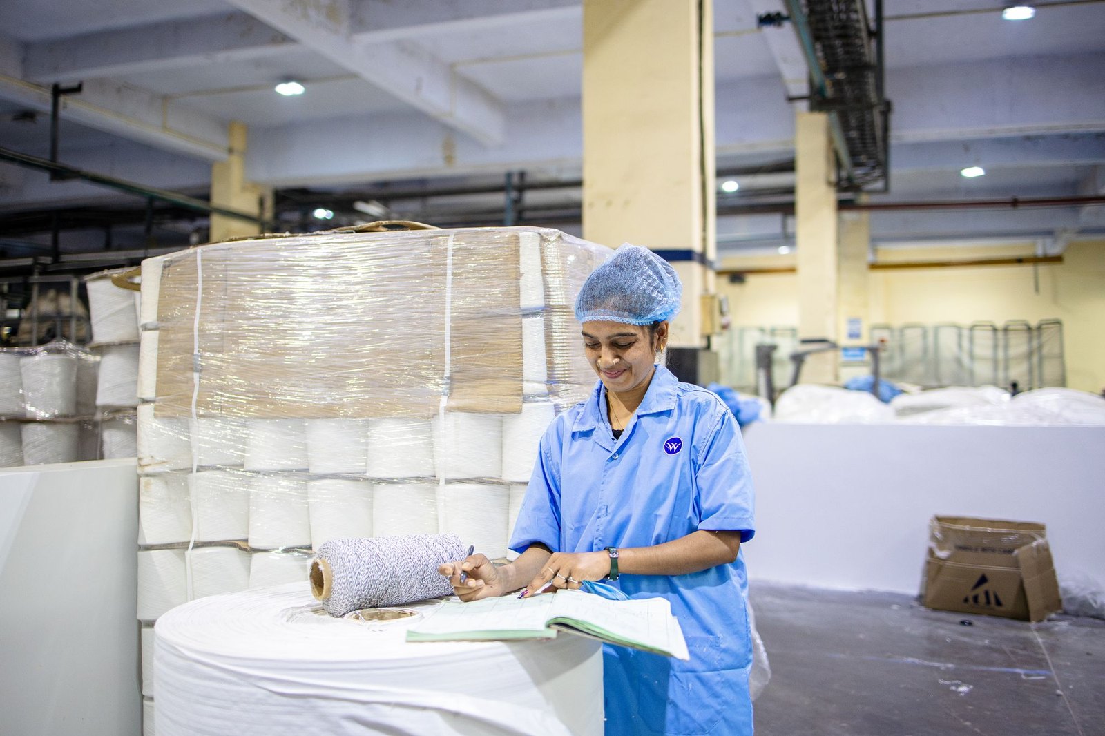Worker recording production specifications in an Indian manufacturing plant, representing substrate spec verification before a converting run