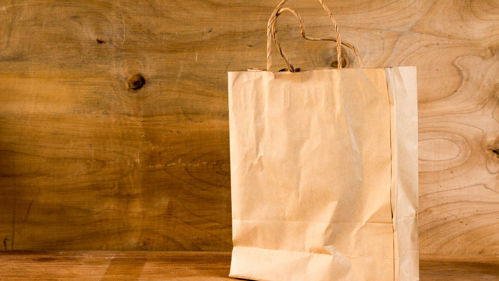 Brown unbleached kraft paper carry bag with twisted handles on a wooden surface