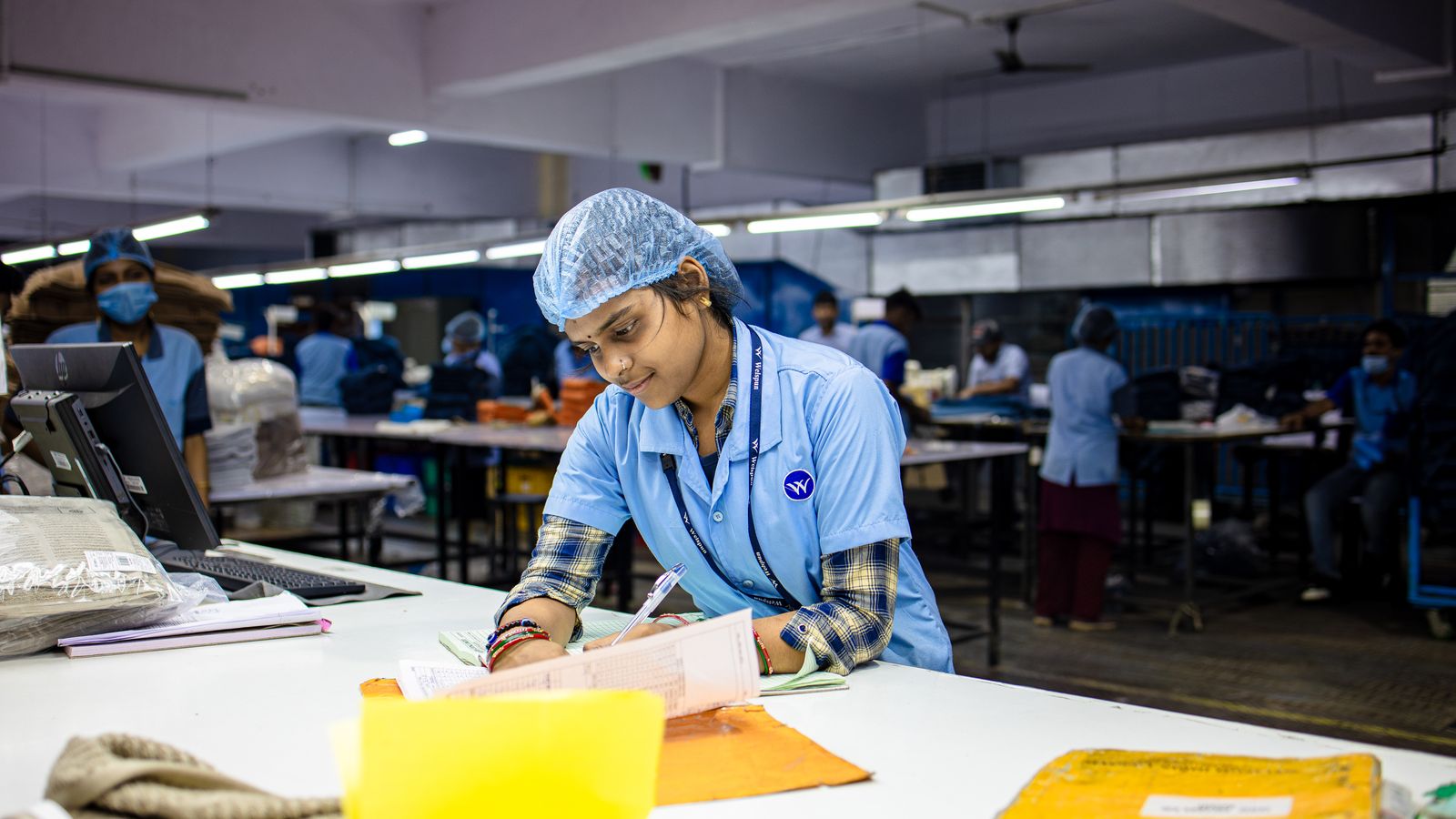 Indian factory worker in uniform and hairnet recording quality-control results at a workstation