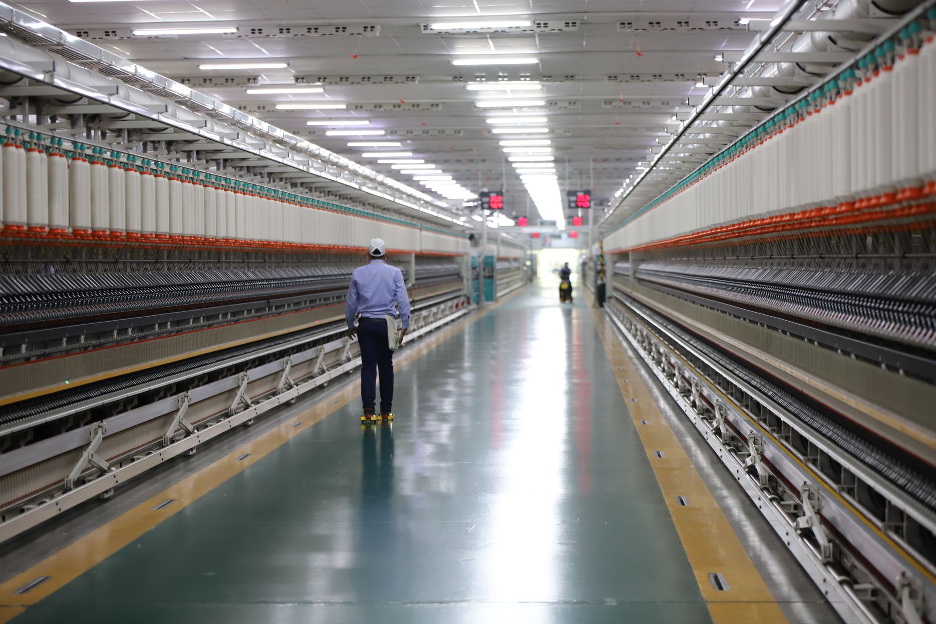 A worker walking a wide aisle in an Indian industrial mill lined with production machinery and reel stock