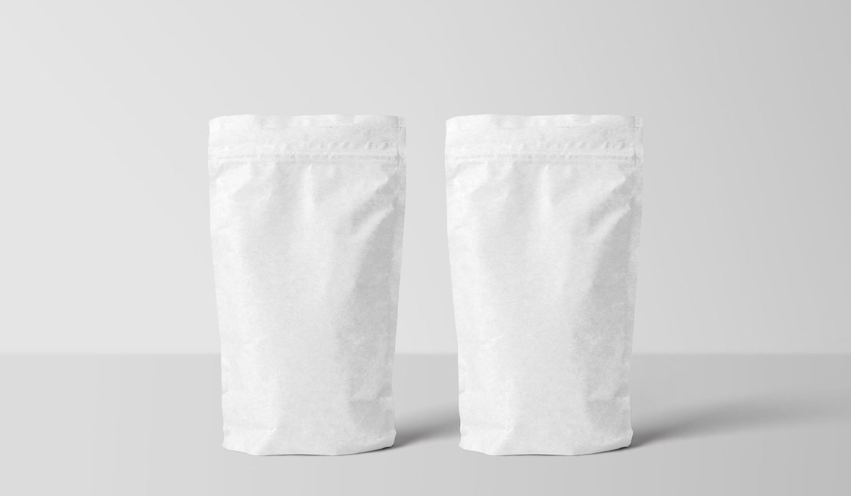 Two blank white stand-up pouches with a paper-look finish on a plain grey background
