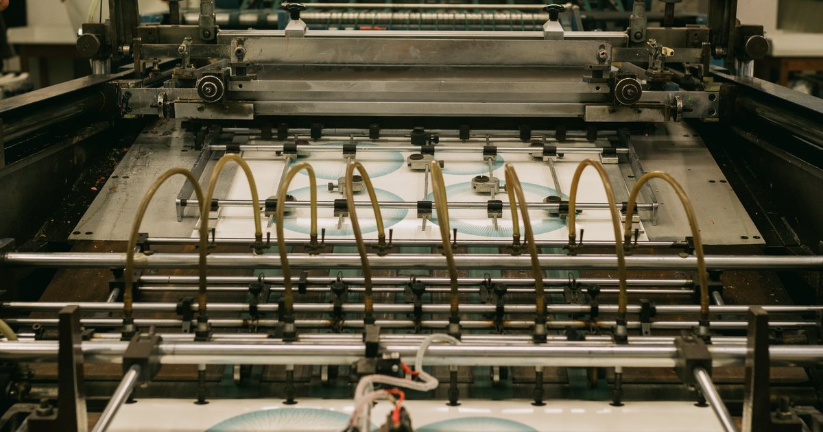 Printed paper sheets passing through the feeder of a sheet-fed printing press, with guide rails and suction tubes above the sheet