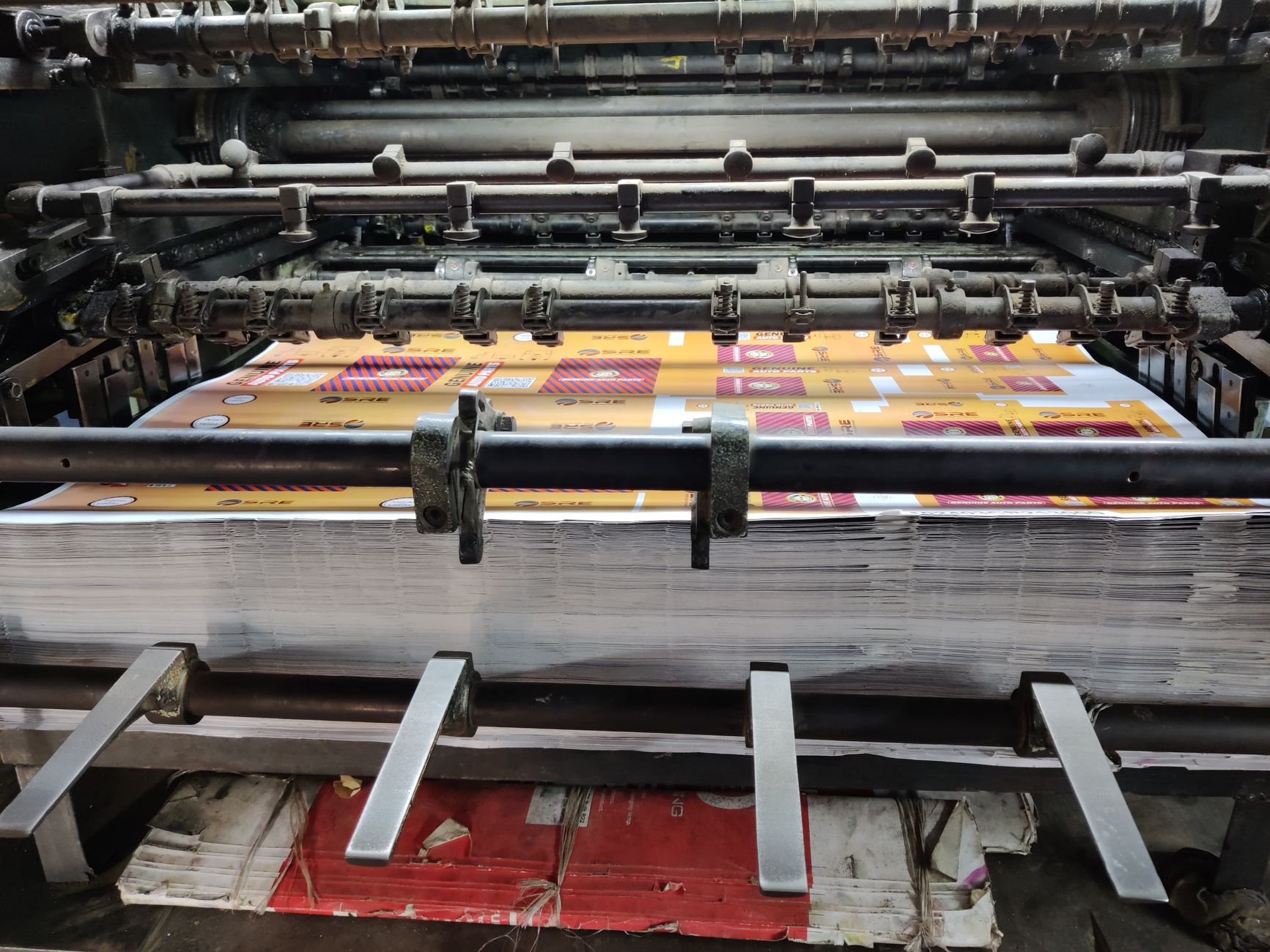 Close-up of an industrial press running paper sheets through nip rollers, the coating stage where silicone is applied to a release liner base