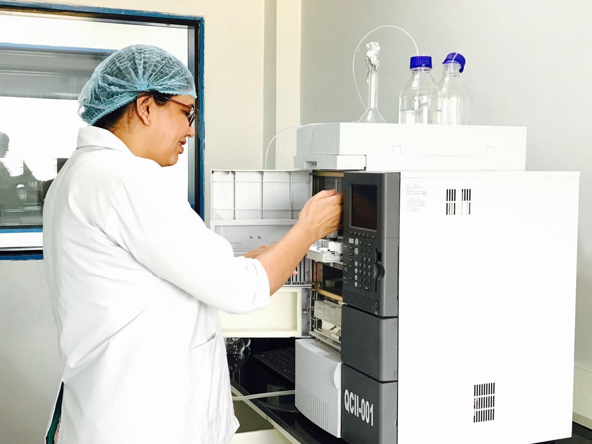 Laboratory analyst in a hairnet and white coat loading a sample into an analytical instrument in a quality-control lab