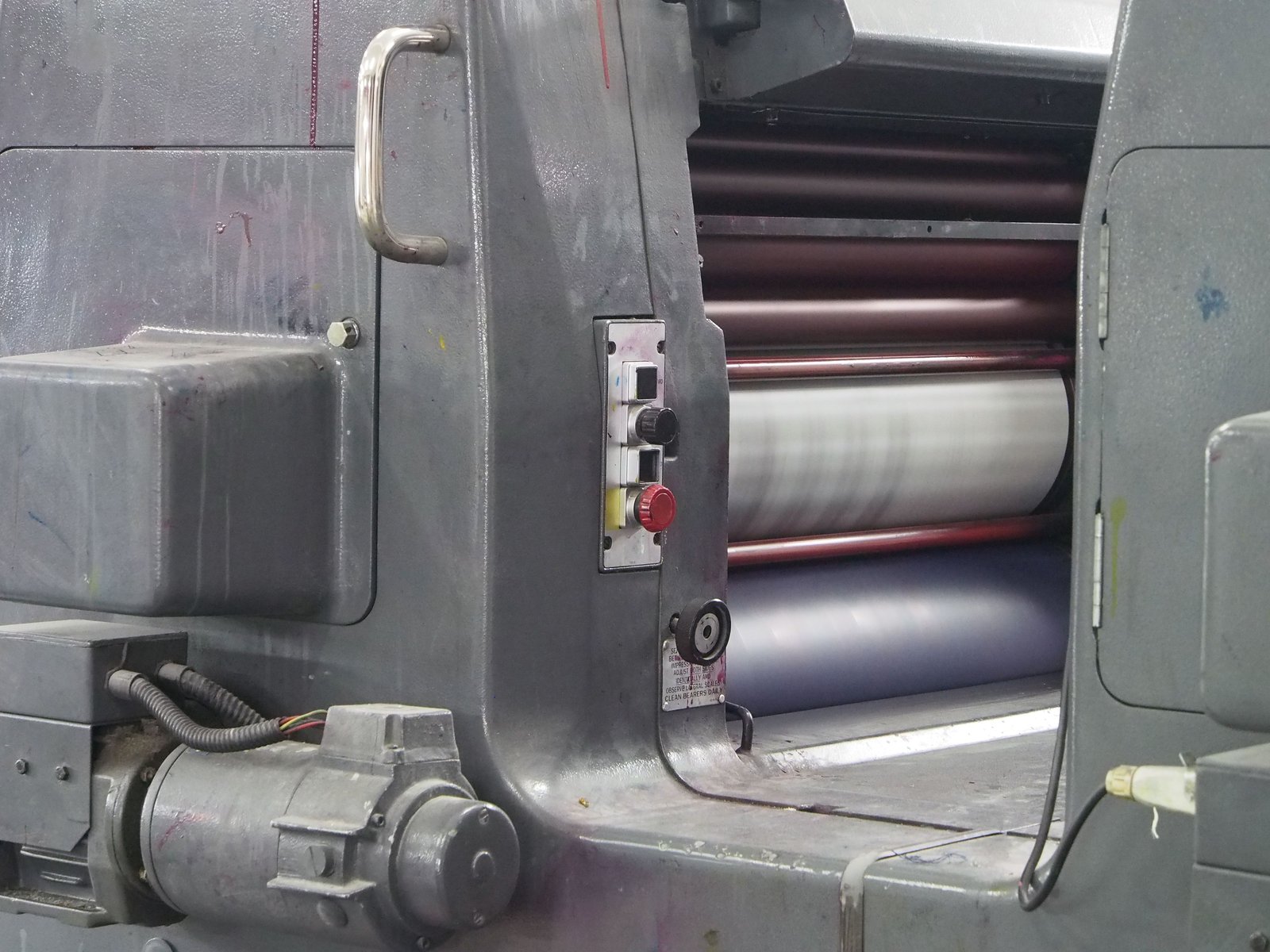 Inking rollers and the impression cylinder of a web printing press seen through the side frame, with the control panel in the foreground