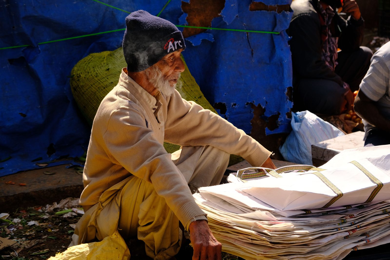 Elderly trader at a Bengaluru market sitting beside stacks of folded used paper bags