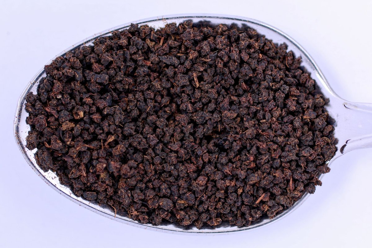 Close view of granular black CTC tea on a clear spoon against a white background