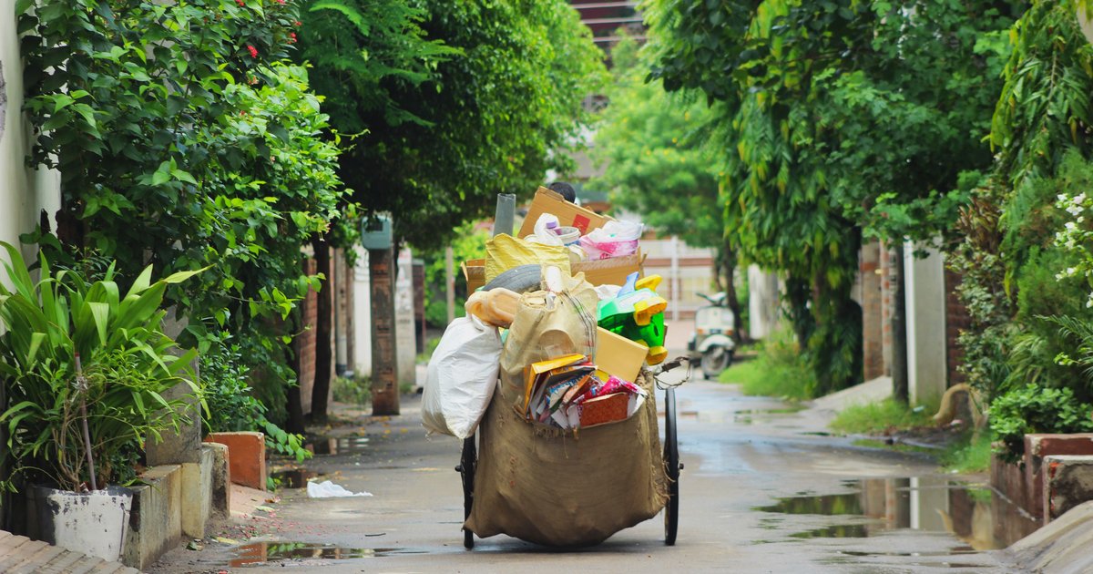 Hand cart piled with used cartons, plastic bags and mixed packaging waste on a wet residential lane in Ludhiana, India