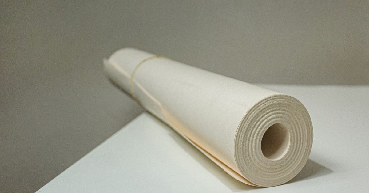 Loosely rolled sheet of plain off-white paper held with a rubber band, lying on a white surface