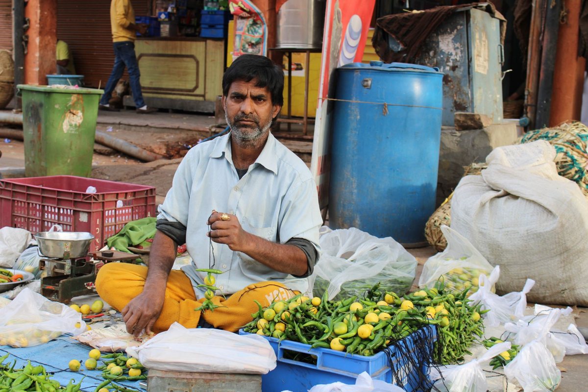 Vegetable vendor in a Jaipur market selling green chillies and lemons, with thin plastic bags beside his stock