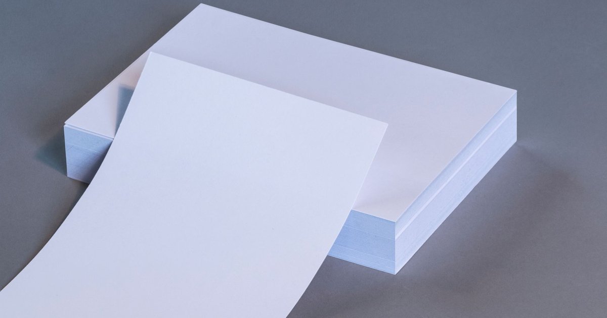 A curved sheet of bright white paper resting on a thick stack of white paper sheets on a grey surface